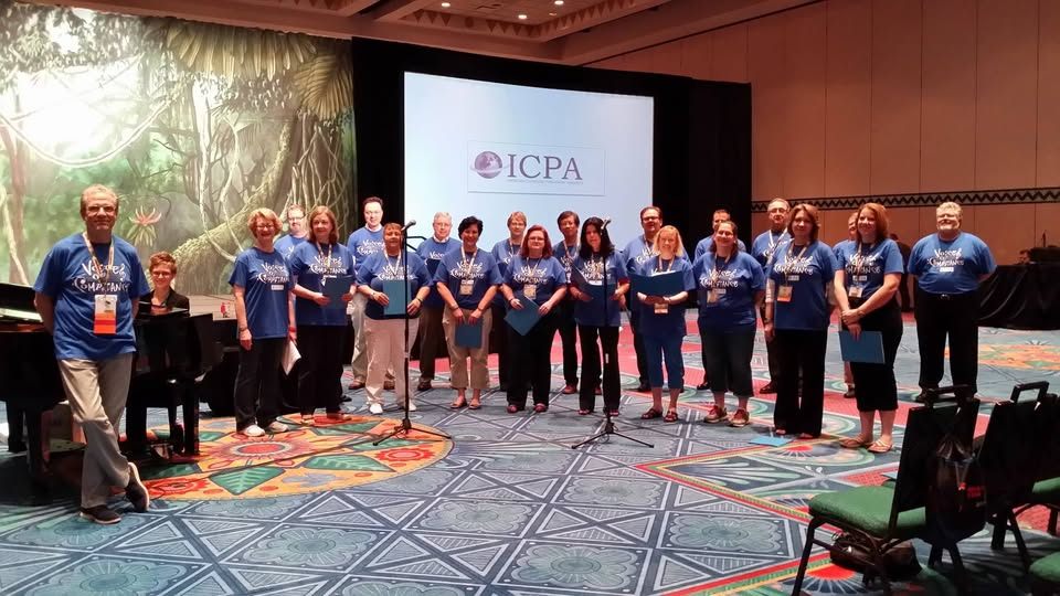 The choir standing in a line in blue shirts in front of a screen showing the ICPA logo.