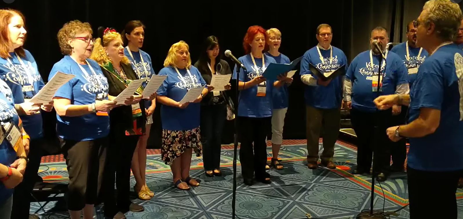 Members of the Voices of Compliance choir singing from sheet music at an ICPA conference.
