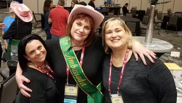 Three ICPA volunteers standing arm in arm at a conference reception, one wearing an ambassador sash