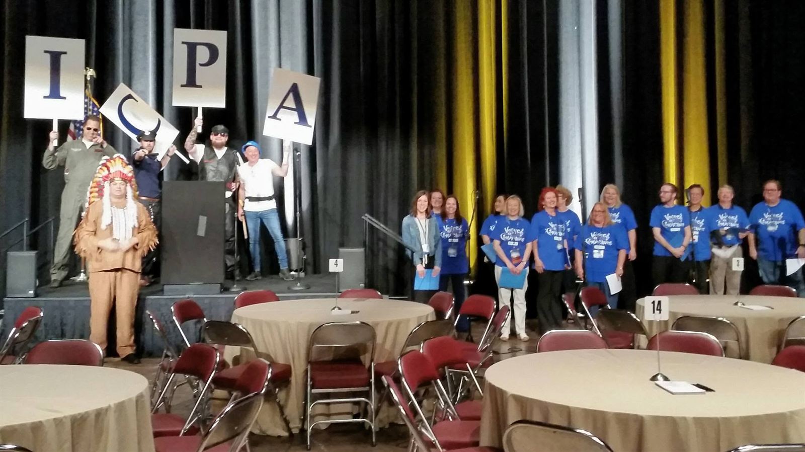 Costumed members holding letter cards spelling I-C-P-A on stage while the choir looks on.